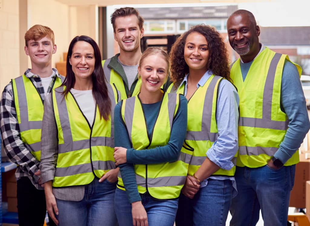 Multi-Cultural Team Wearing Hi-Vis Safety Clothing Working In Modern Warehouse